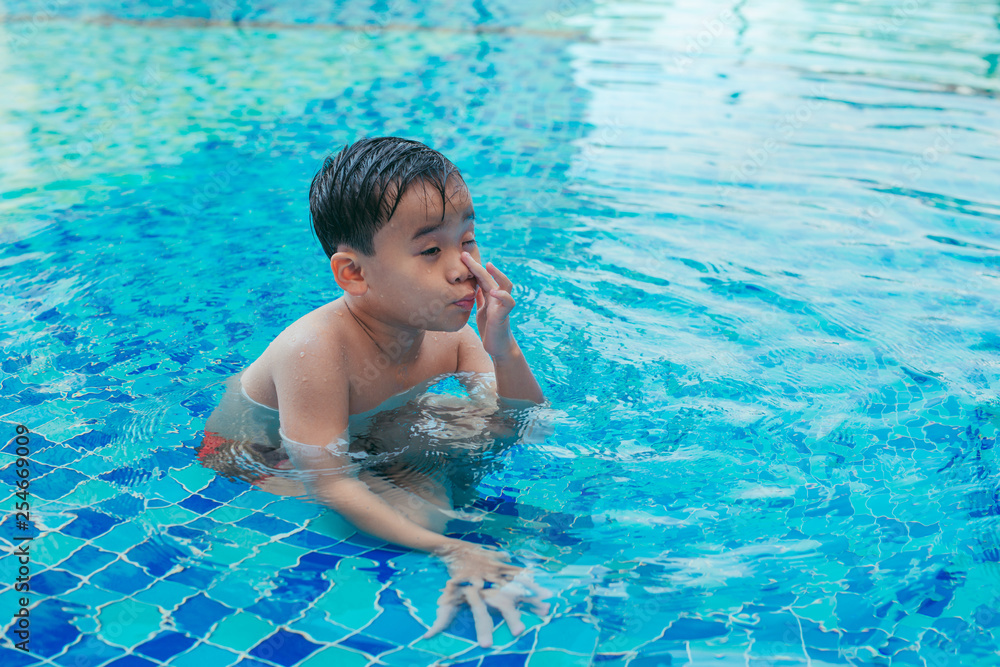 Child at the swimming pool steps, rubbing water from his eyes.
