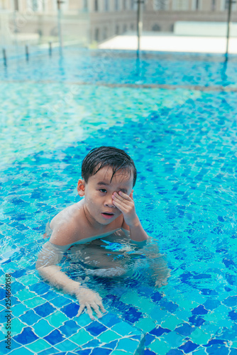 Child at the swimming pool steps, rubbing water from his eyes.