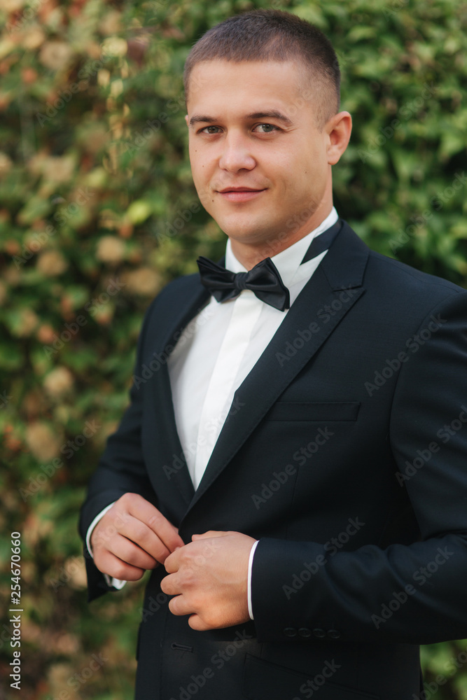 Young groom in suit otside. Handsome man in black suit. Model walking in the park Young groom in suit otside. Handsome man in black suit. Model walking in the park