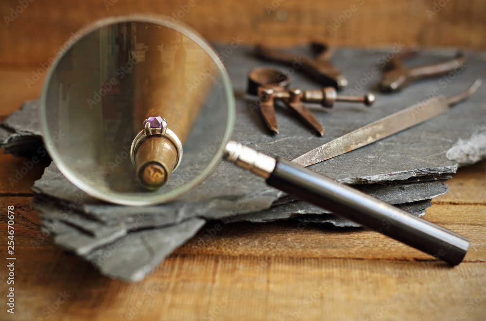 Ring, magnifying glass and jeweler tools on blackboard
