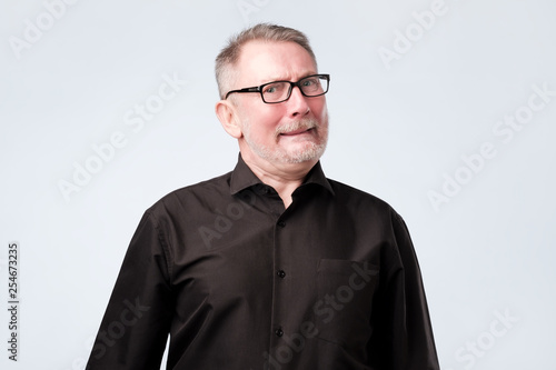 Caucasian senior grandfather curves lips, looks doubtfully, thinks what to do.