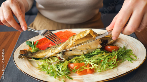 Close up of woman eating fish steak with knife and fork.