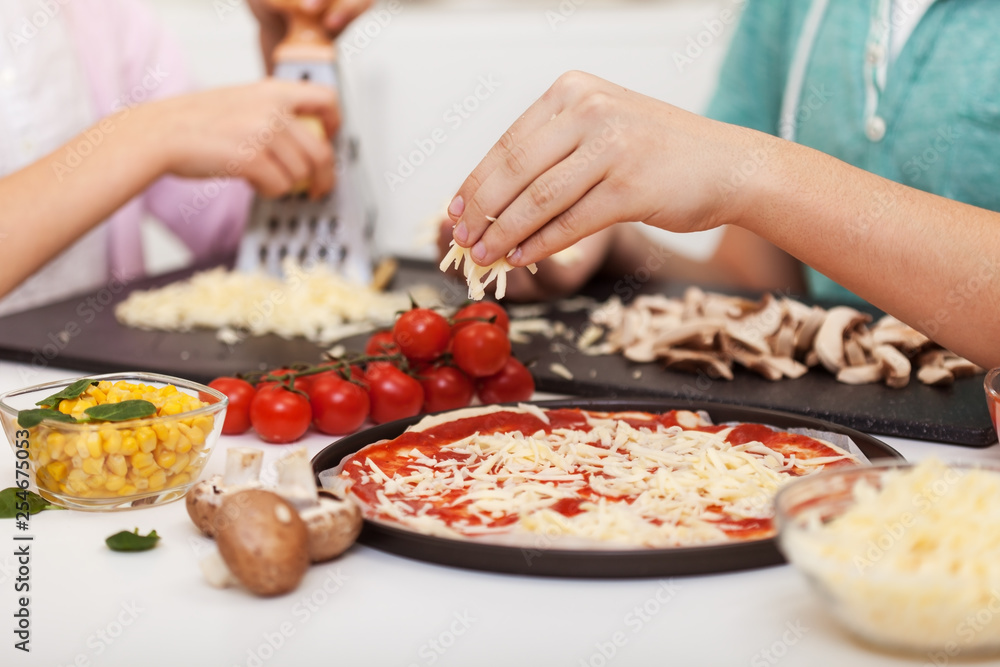 Young hands prepare pizza at home - grate and sprinkle the cheese