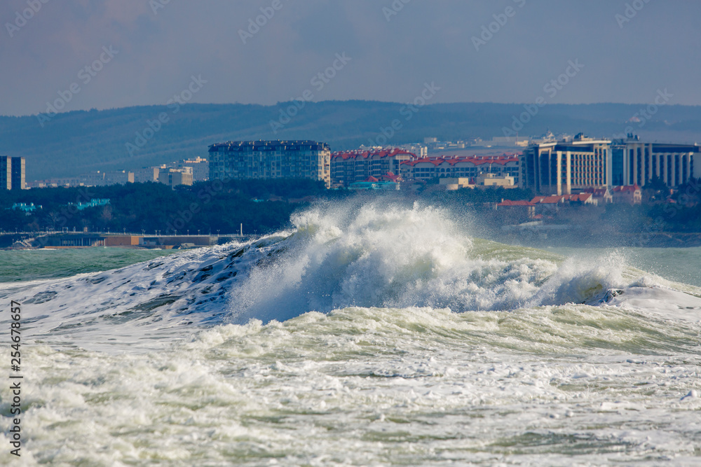 Strong and dangerous storm in the Black sea. Beautiful and big storm wave in Gelendzhik Bay on the background of the resort of Gelendzhik, waterfront and lighthouse. In the background, hotels