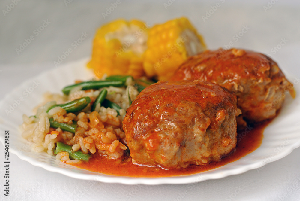 Meat cutlets with tomato sauce, rice and vegetables on a white ceramic plate. Close-up