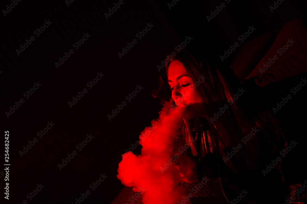 Girl model smokes vape in red light. Girl model smokes vape in red light.