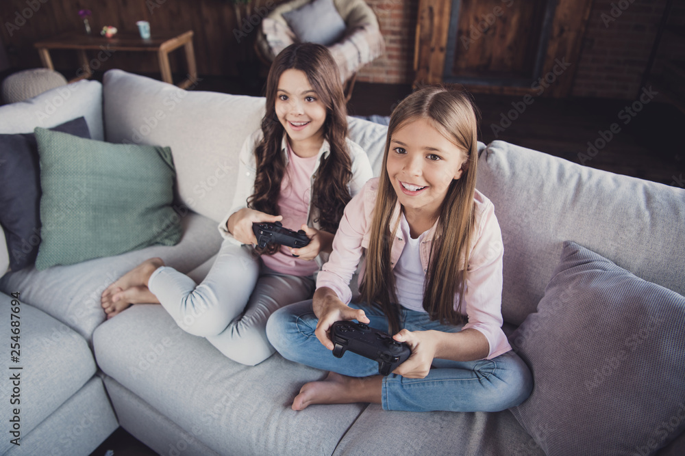 Above high angle view portrait of two nice lovely sweet attractive charming cheerful cheery positive girls sitting on divan playing video game battle crossed legs in house loft industrial interior Above high angle view portrait of two nice lovely sweet attractive charming cheerful cheery positive girls sitting on divan playing video game battle crossed legs in house loft industrial interior
