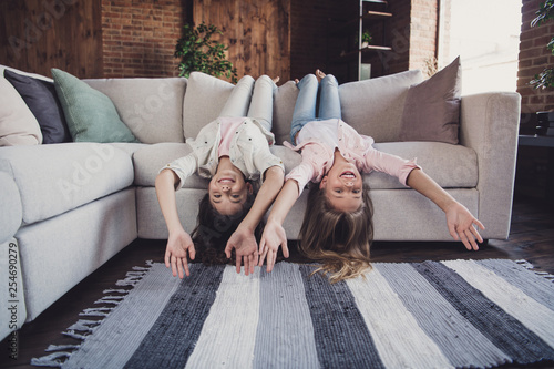 Two nice lovely attractive charming different cheerful cheery friendly girls lying on divan upside-down having fun day in house loft industrial interior style