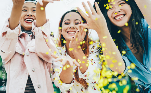 Happy Asian friends having fun throwing confetti outdoor - Young trendy people celebrating at festival event outside - Party, entertainment and youth holidays lifestyle concept
