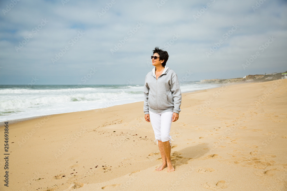 Portrait of a Happy mature woman walking on the Ocean Beach. Enjoying Freedom of Travel Vacation. Wellness and Happiness Lifestyle Concept. Portugal. Santa Cruz Portrait of a Happy mature woman walking on the Ocean Beach. Enjoying Freedom of Travel Vacation. Wellness and Happiness Lifestyle Concept. Portugal. Santa Cruz