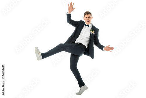 cheerful groom dancing in white sneakers and looking at camera isolated on white