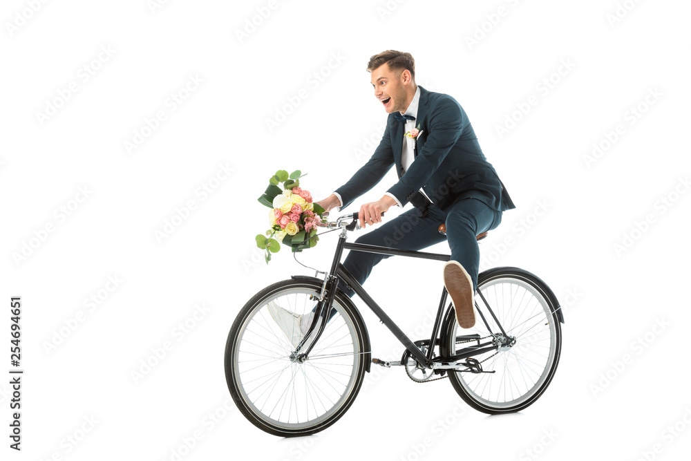 happy groom in elegant suit and sneakers riding bike while holding wedding bouquet isolated on white happy groom in elegant suit and sneakers riding bike while holding wedding bouquet isolated on white