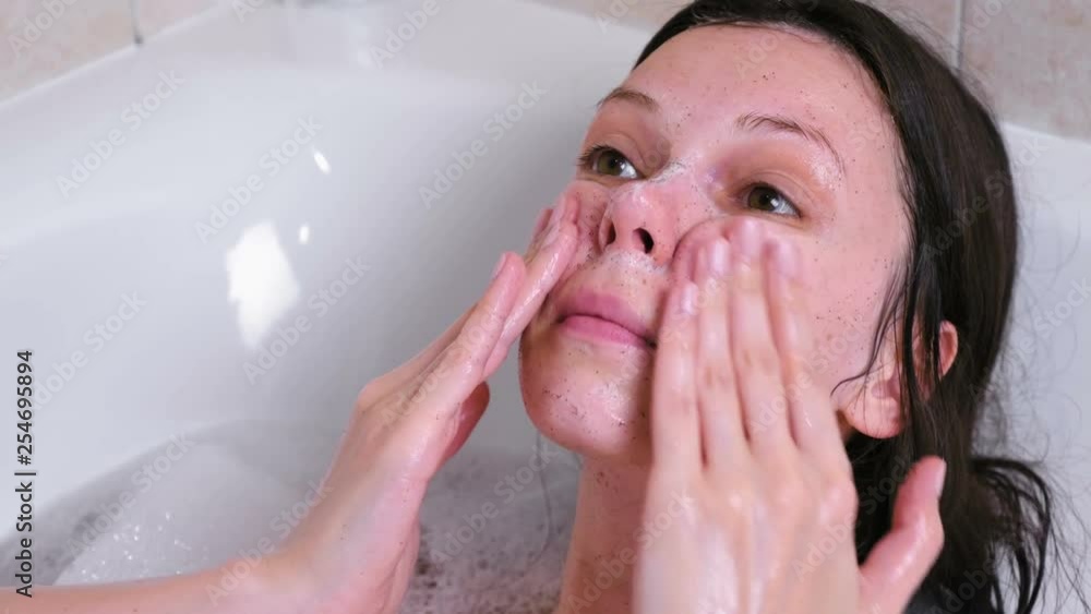 Beautiful brunette woman puts a scrub on the face lying in the bathroom. Face close-up. Beautiful brunette woman puts a scrub on the face lying in the bathroom. Face close-up.
