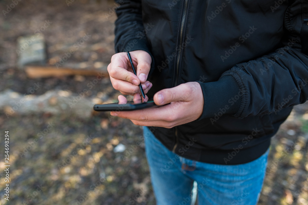 Fototapeta premium Young man wearing jeans using a modern smartphone with stylus, focus on the hands.