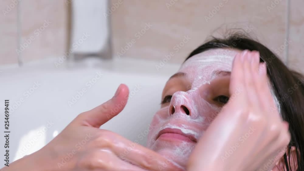 Beautiful brunette woman puts a mask on the face lying in the bathroom at home. Face close-up. Beautiful brunette woman puts a mask on the face lying in the bathroom at home. Face close-up.