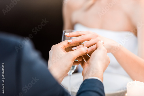 selective focus of man putting wedding ring on brides finger on black background