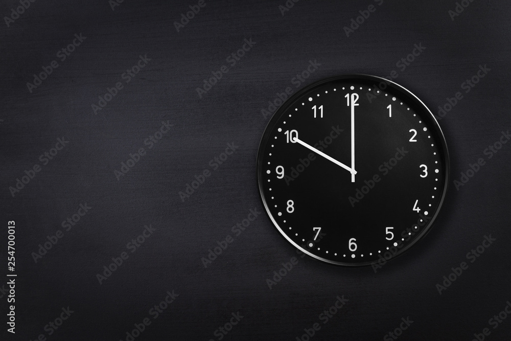 Black wall clock showing ten o'clock on black chalkboard background