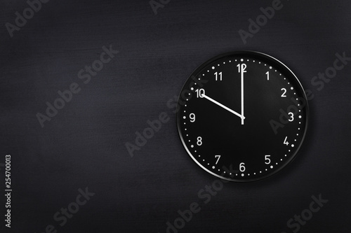Black wall clock showing ten o'clock on black chalkboard background. Office clock showing 10am or 10pm on black texture photo