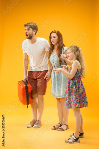 Sad unhappy parent with daughter and suitcase at studio isolated on yellow background. Travel, vacation, parenthood, togetherness, tourism concept. © master1305