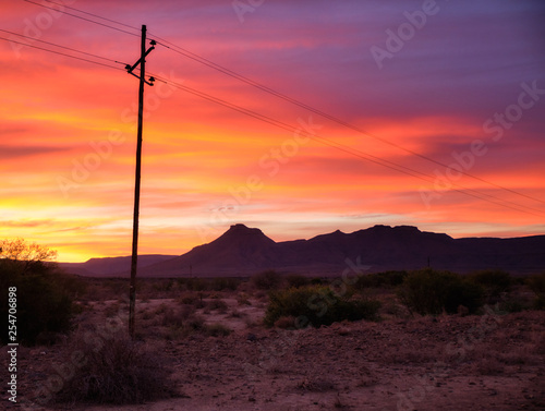 Sunset sky of orange and yellow in the vast  Karoo of South Africa. With silhouette of telephone pole and wires leading to mountain range