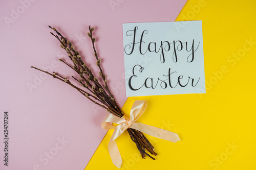 Willow branches and Happy Ester greeting card isolated on yellow and pink background. Spring and Easter concept. Top view