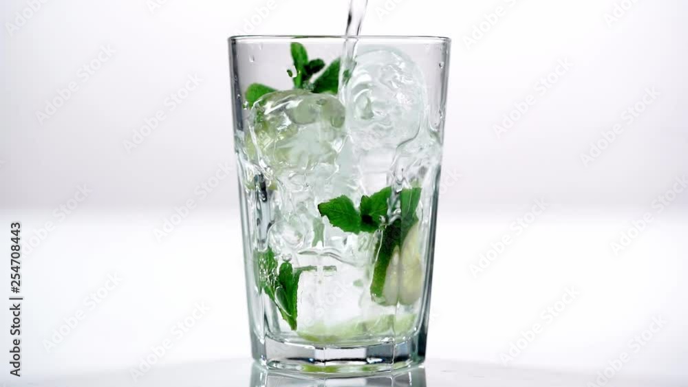studio shoot of clear water pouring in glass with green mint leaves, lime slices and ice cubes on white background studio shoot of clear water pouring in glass with green mint leaves, lime slices and ice cubes on white background