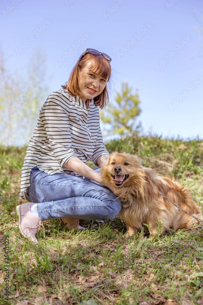 Fototapeta girl in blue jeans and striped jumper with a dog on the edge of the spring forest