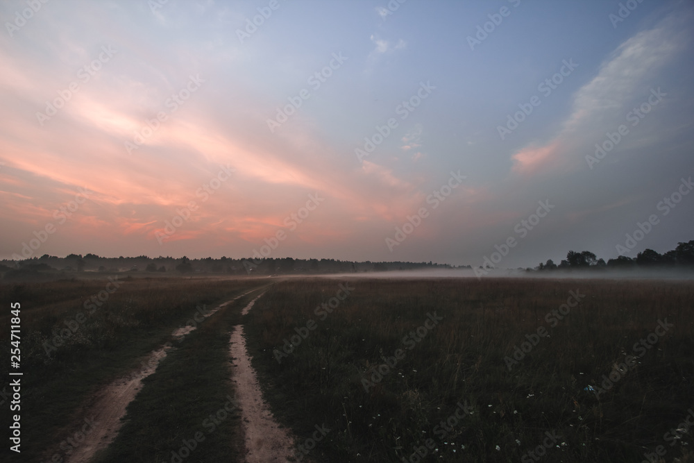 Sunrise on the fields with fog, rural road.