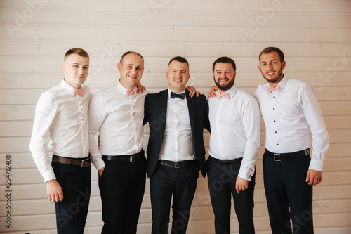 Handsome groom with his groomsman at home. Five man. Groom dressed in suit, gromsmen in white shirt. Funny guys on the wedding photo