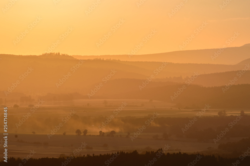 A moody sunset over a mountain range, fields shrouded in fog. A moody sunset over a mountain range, fields shrouded in fog.