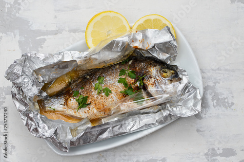 baked fish with lemon in aluminium foil on ceramic background