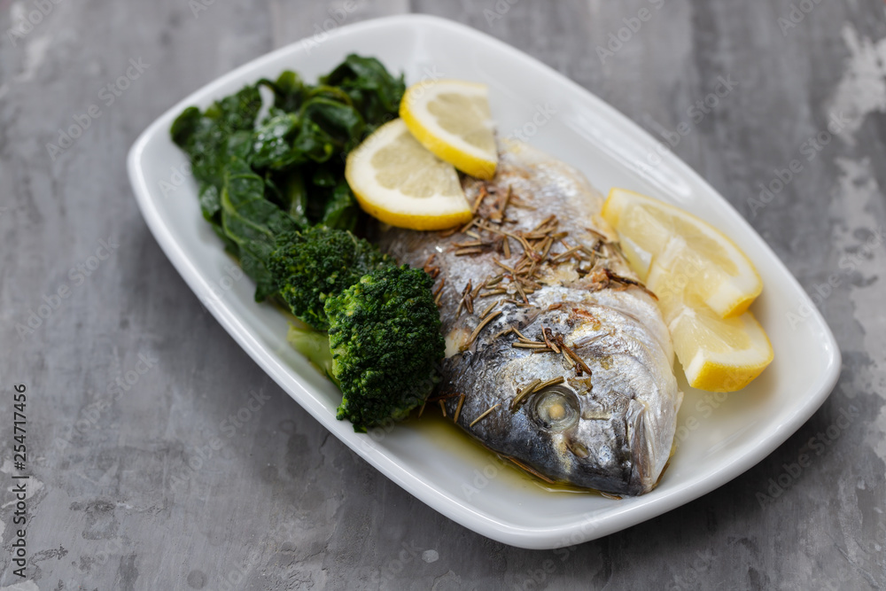 baked fish with lemon and vegetables in white dish on ceramic background baked fish with lemon and vegetables in white dish on ceramic background