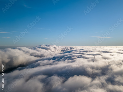 View of a drone above the fog, wind turbines with fog and blue sky