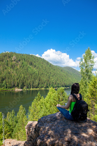 Young traveling woman sitting on the top of the mountain cliff.