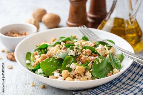 Healthy salad with spinach, chickpeas, quinoa, feta cheese and walnuts in white plate on concrete background. Selective focus.