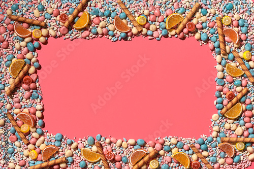 Multicolored glazed dragees and other sweets are arranged in the form of a frame on a coral background.