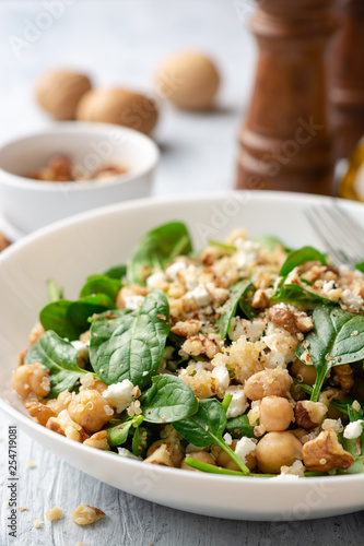 Healthy salad with spinach, chickpeas, quinoa, feta cheese and walnuts in white plate on concrete background. Selective focus.