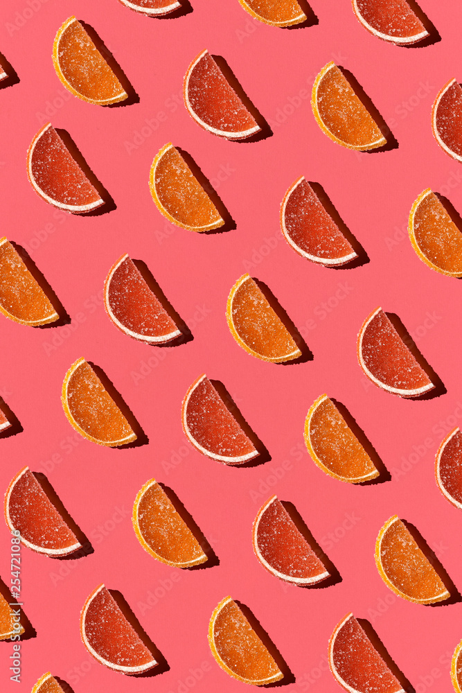 Fototapeta premium Pattern made of colorful candied fruits orange lemon on coral background. Flat lay. Minimal concept