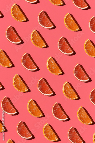 Pattern made of colorful candied fruits orange lemon on coral background. Flat lay. Minimal concept