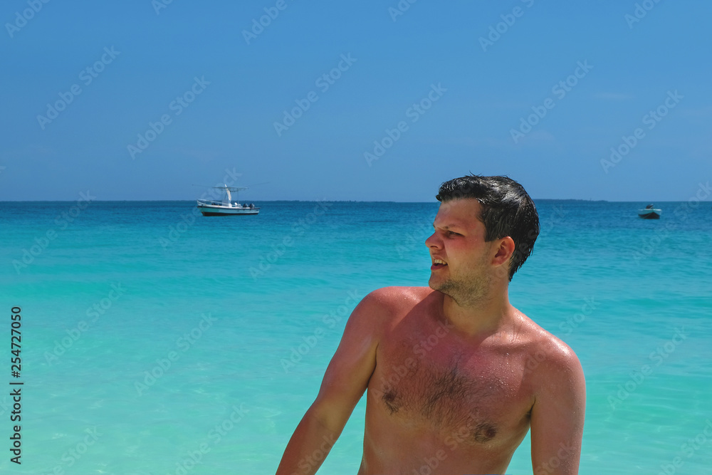Young attractive man winces after sunburn while standing in turquoise water Young attractive man winces after sunburn while standing in turquoise water