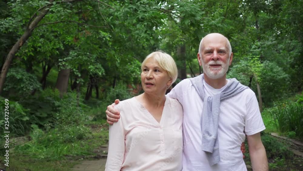Senior couple walking in summer park embracing. Active modern life after retirement. Happy family enjoying time together in green garden Senior couple walking in summer park embracing. Active modern life after retirement. Happy family enjoying time together in green garden