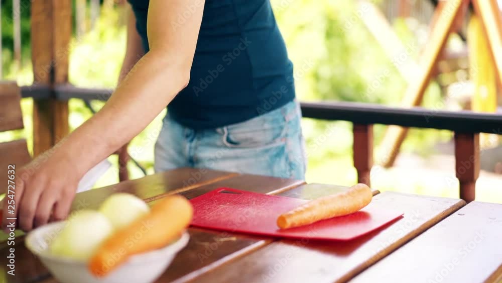 CU, Travelling shot: guy is standing in summer house, cooking pilaf, for picnic. He cuts carrots, on red cutting board. CU, Travelling shot: guy is standing in summer house, cooking pilaf, for picnic. He cuts carrots, on red cutting board.