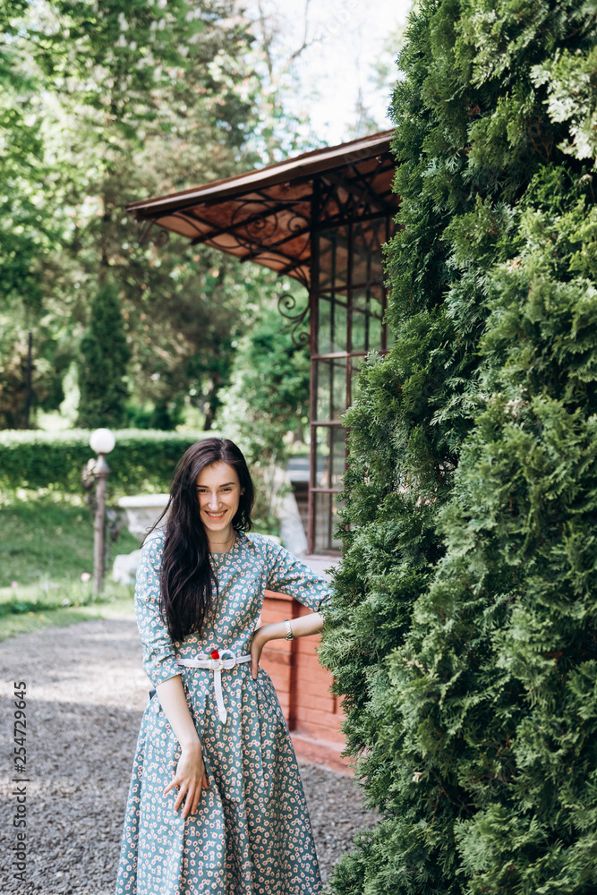 Naklejka premium Happy attractive young smiling woman in cute summer dress with flower print in the garden
