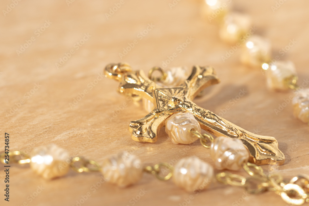 A white rosary with a golden cross on a wooden table. A white rosary with a golden cross on a wooden table.