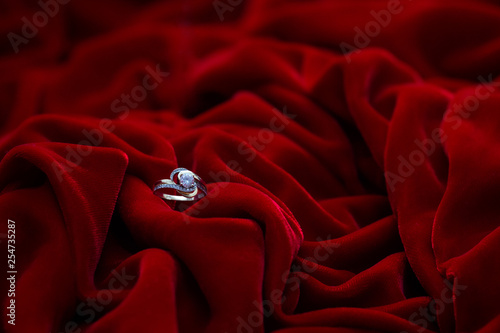 Golden engagement ring with diamond. Special jewelry design. Red soft velor fabric in folds and drapes. The wedding ring is in red fabric.