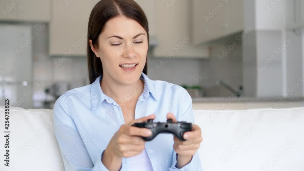 Brunette woman gamer sitting in living room playing video games at home. Addicted female player with remote controller of game console. Сoncept of winning in cybersport