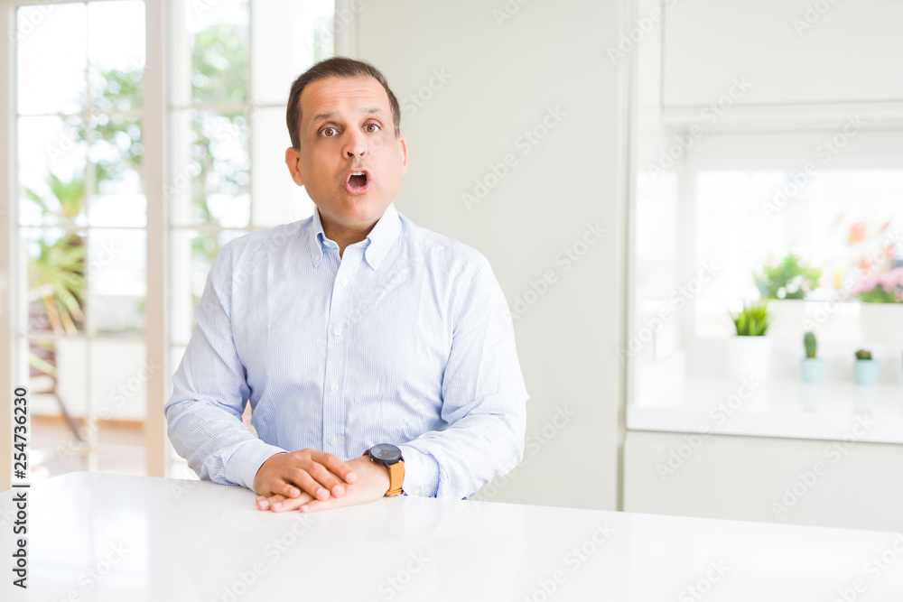 Middle age man sitting at home afraid and shocked with surprise expression, fear and excited face.