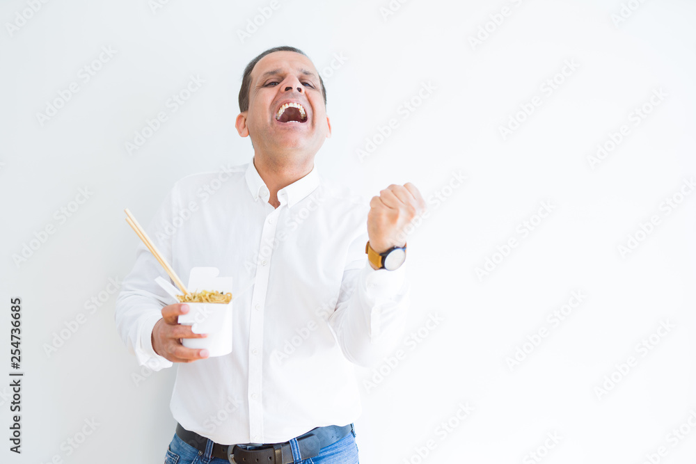 Middle age man eating asian noodles from take away carton screaming proud and celebrating victory and success very excited, cheering emotion Middle age man eating asian noodles from take away carton screaming proud and celebrating victory and success very excited, cheering emotion