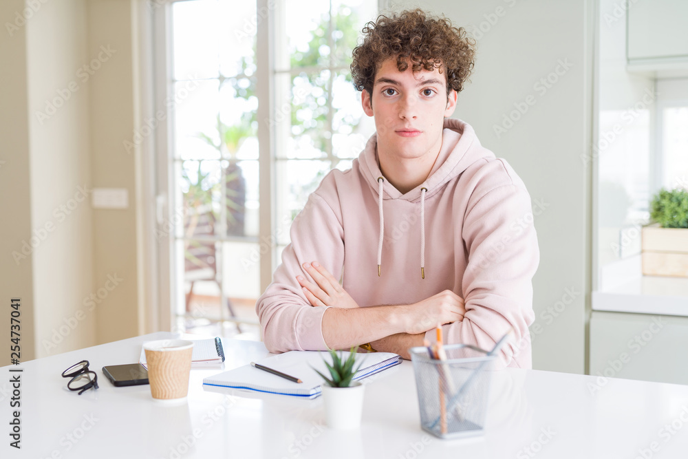 Fototapeta premium Young student man writing on notebook and studying with serious expression on face. Simple and natural looking at the camera.