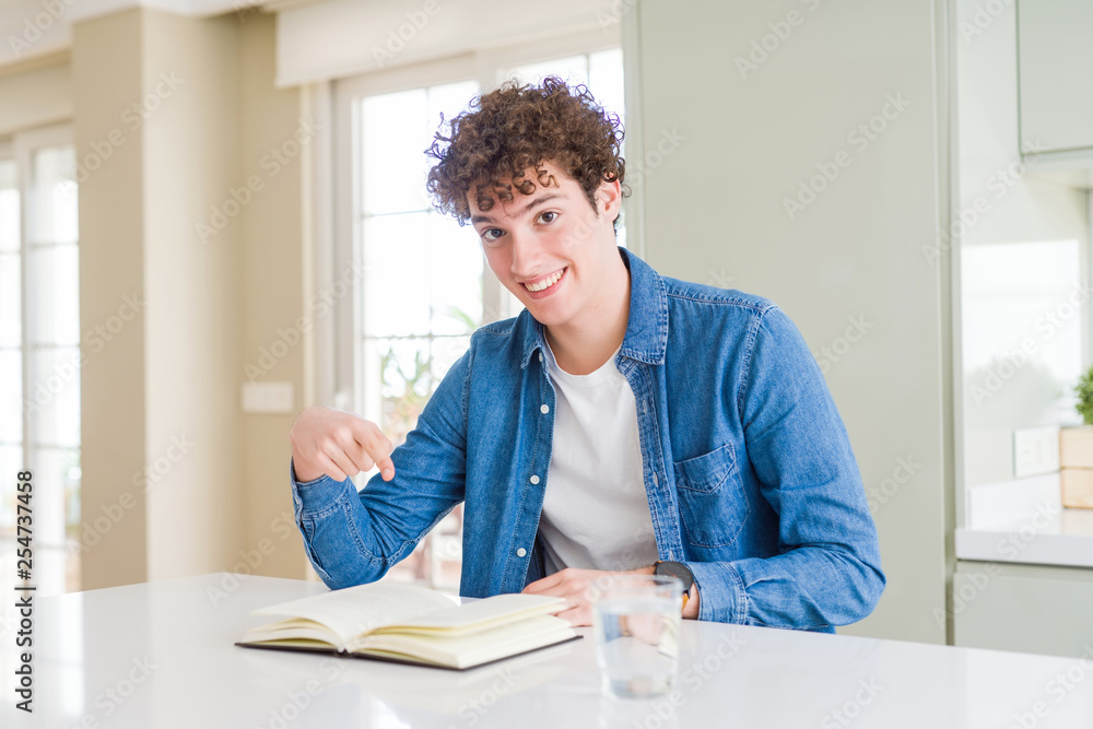 Young man reading a book at home very happy pointing with hand and finger Young man reading a book at home very happy pointing with hand and finger